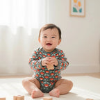 Baby sitting on a light-colored floor wearing a patterned onesie.