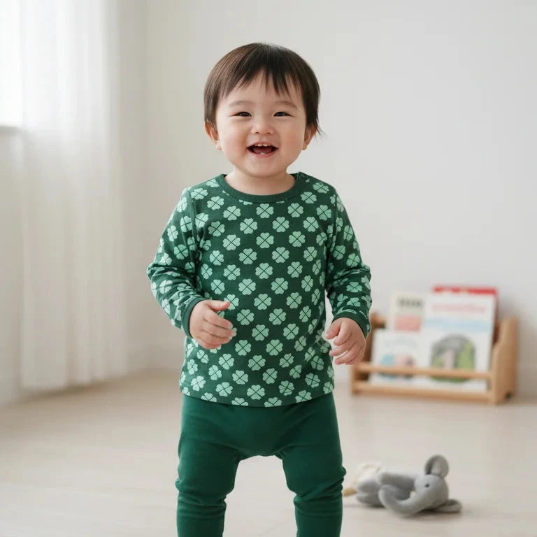 Child wearing a green patterned shirt and pants in a room with a bookshelf and toy.