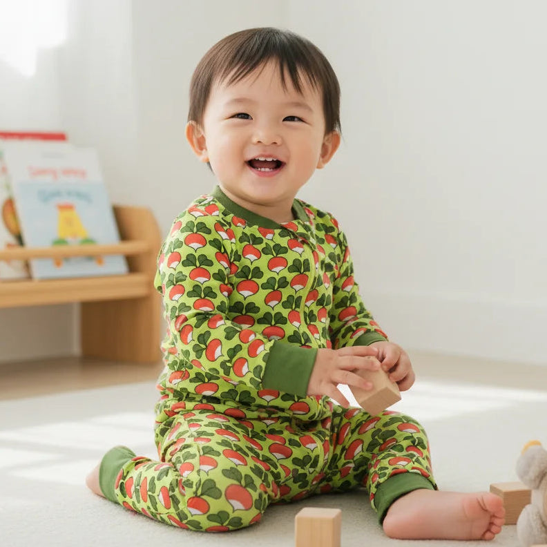 Child wearing a green pajama with red patterns sitting on a white floor.