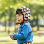 Child wearing a colorful helmet and patterned pants standing in a park.