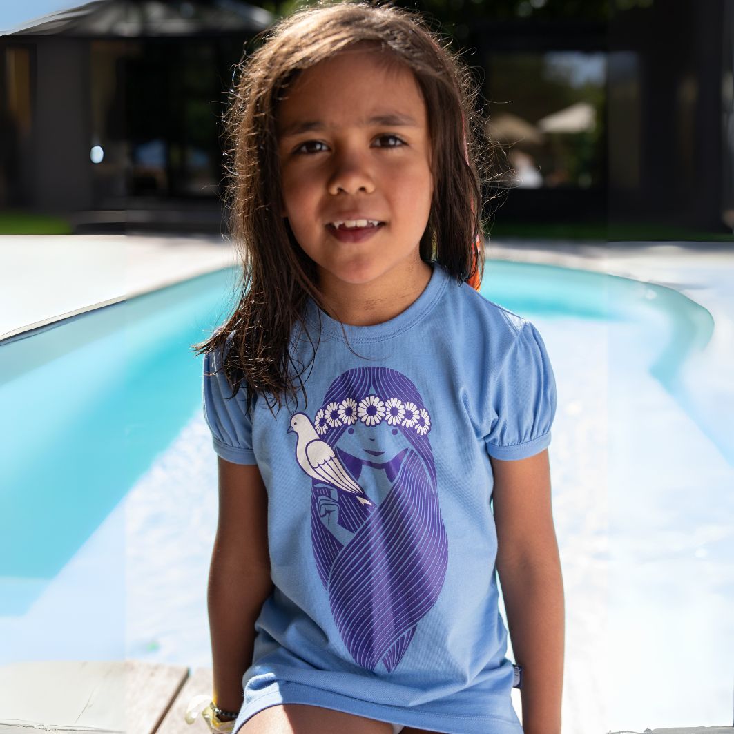 Young girl wearing a blue t-shirt with a graphic design, standing by a pool.