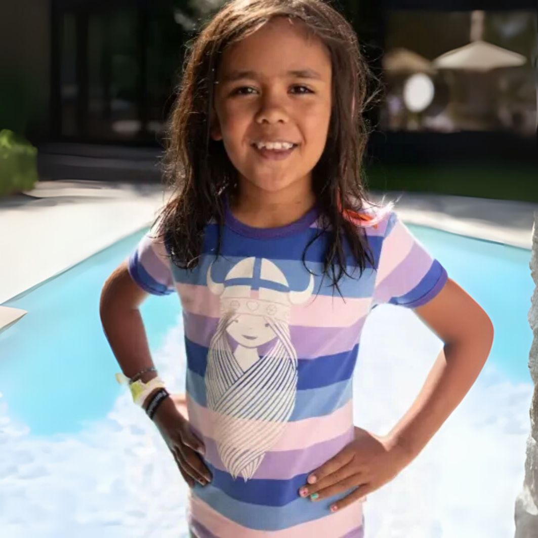 Young girl standing by a pool wearing a colorful striped shirt with a design.