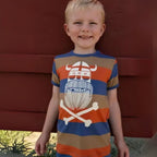 Child wearing a colorful t-shirt with a graphic design against a red wall.