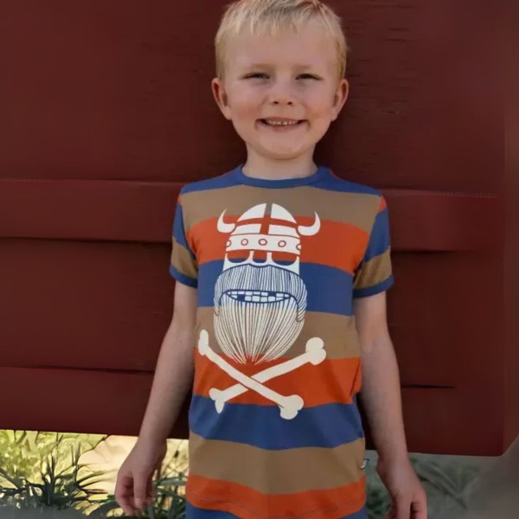 Child wearing a colorful t-shirt with a graphic design against a red wall.