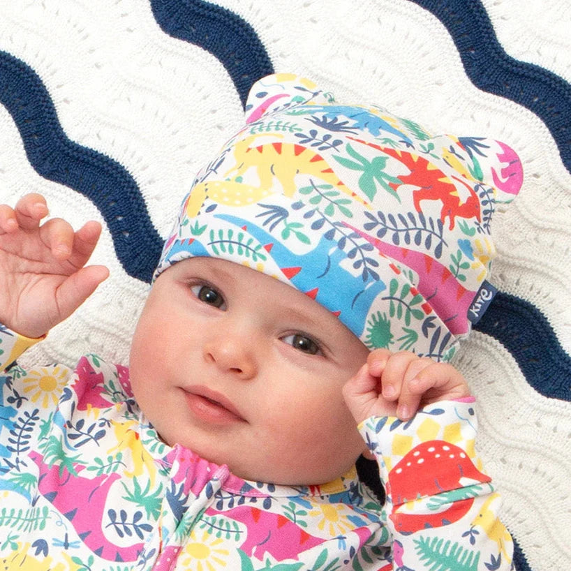 Baby wearing a colorful dinosaur-patterned snowsuit and hat on a striped blanket