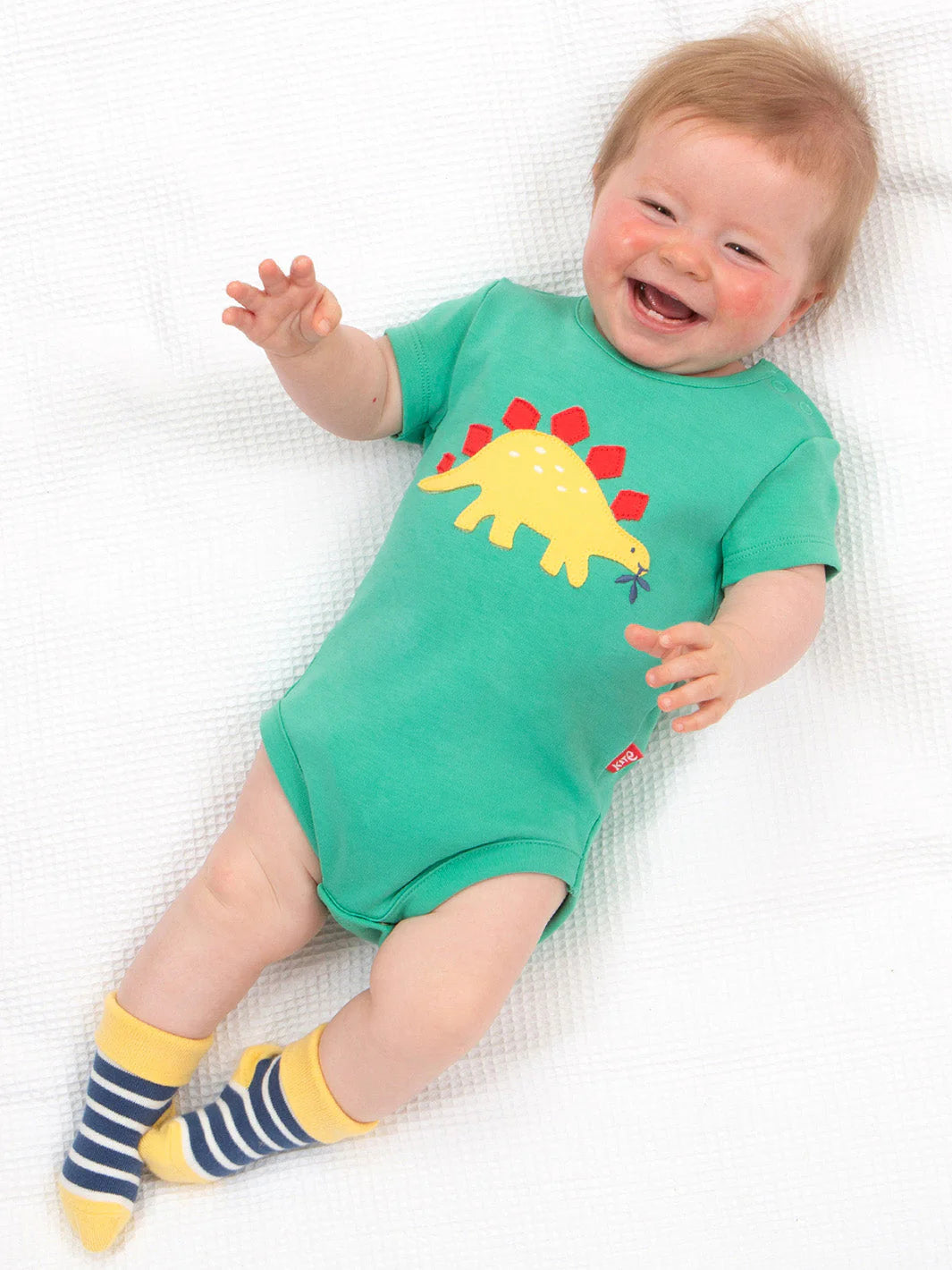 Baby wearing a green onesie with a dinosaur design on a white blanket