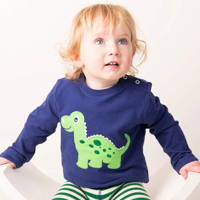 Child wearing a blue shirt with a green dinosaur design and green and white striped pants.