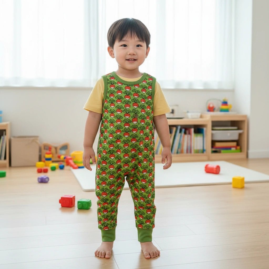 Child wearing a green patterned onesie in a room with toys and books.