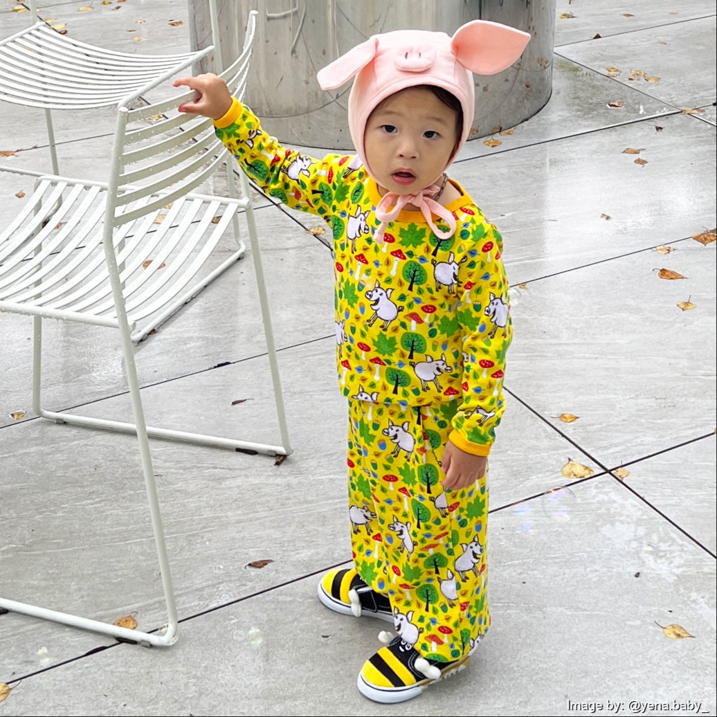 Child wearing a colorful outfit with animal patterns and a pink hat with ears, standing on a concrete floor.