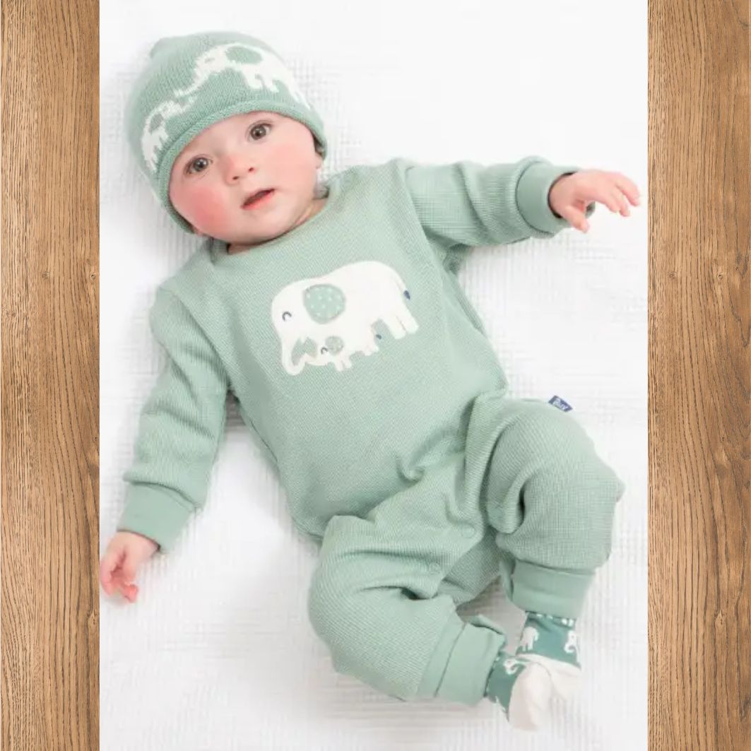 Baby wearing a green outfit with elephant design on a white blanket