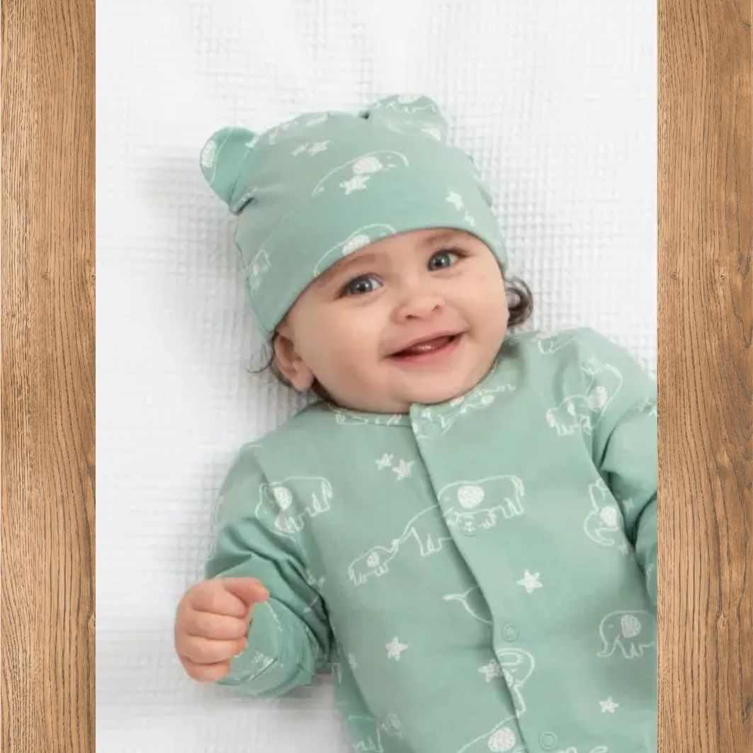 Baby wearing a matching mint green outfit with animal patterns on a white background
