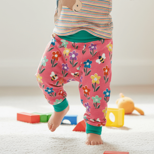 Child in colorful pajamas with a bear design, standing in a room with toys on the floor.