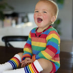 Child wearing a rainbow striped outfit sitting on a couch.