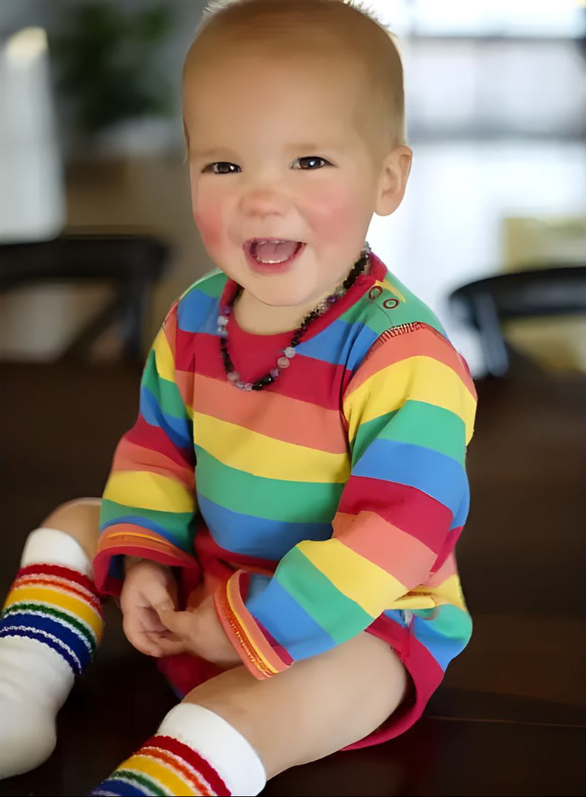 Child wearing a rainbow striped outfit sitting on a couch.