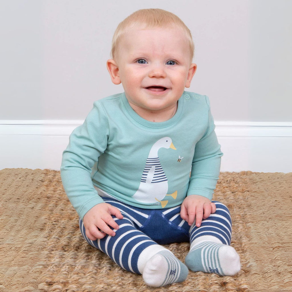 Baby wearing a light blue long-sleeve shirt with a duck design and blue striped pants sitting on a beige carpet.