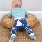 Baby wearing blue and white striped leggings with a duck design, standing on a woven mat.