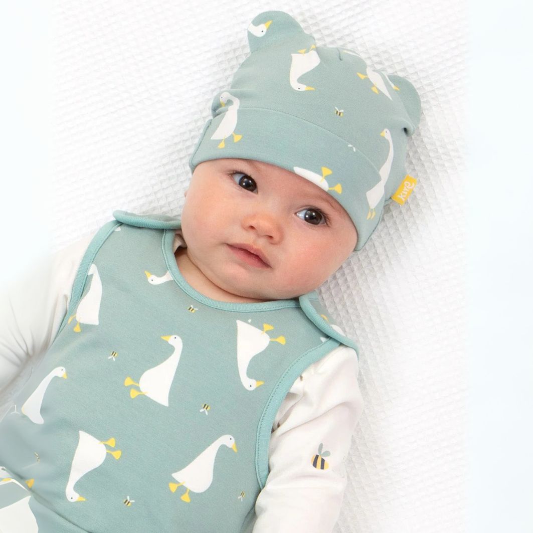 Baby wearing a green outfit with duck pattern and matching hat on a white background
