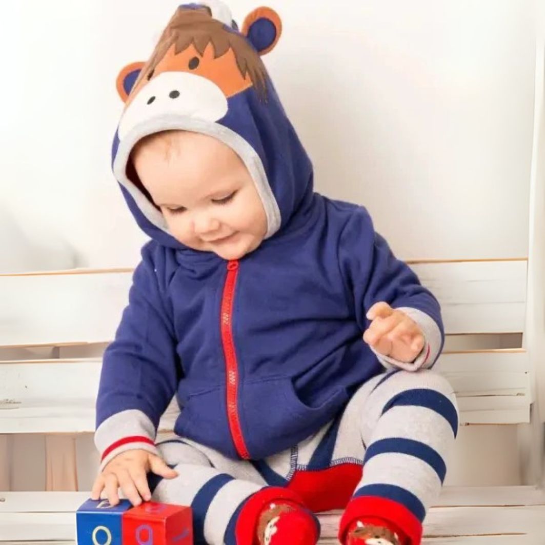 Child wearing a blue animal-themed hoodie with red accents, sitting on a wooden floor.