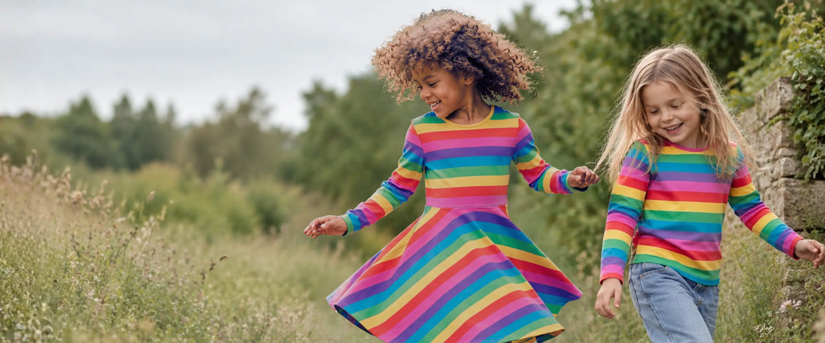 Girl dancing in a Frugi rainbow stripe skater dress on a garden path in soft daylight