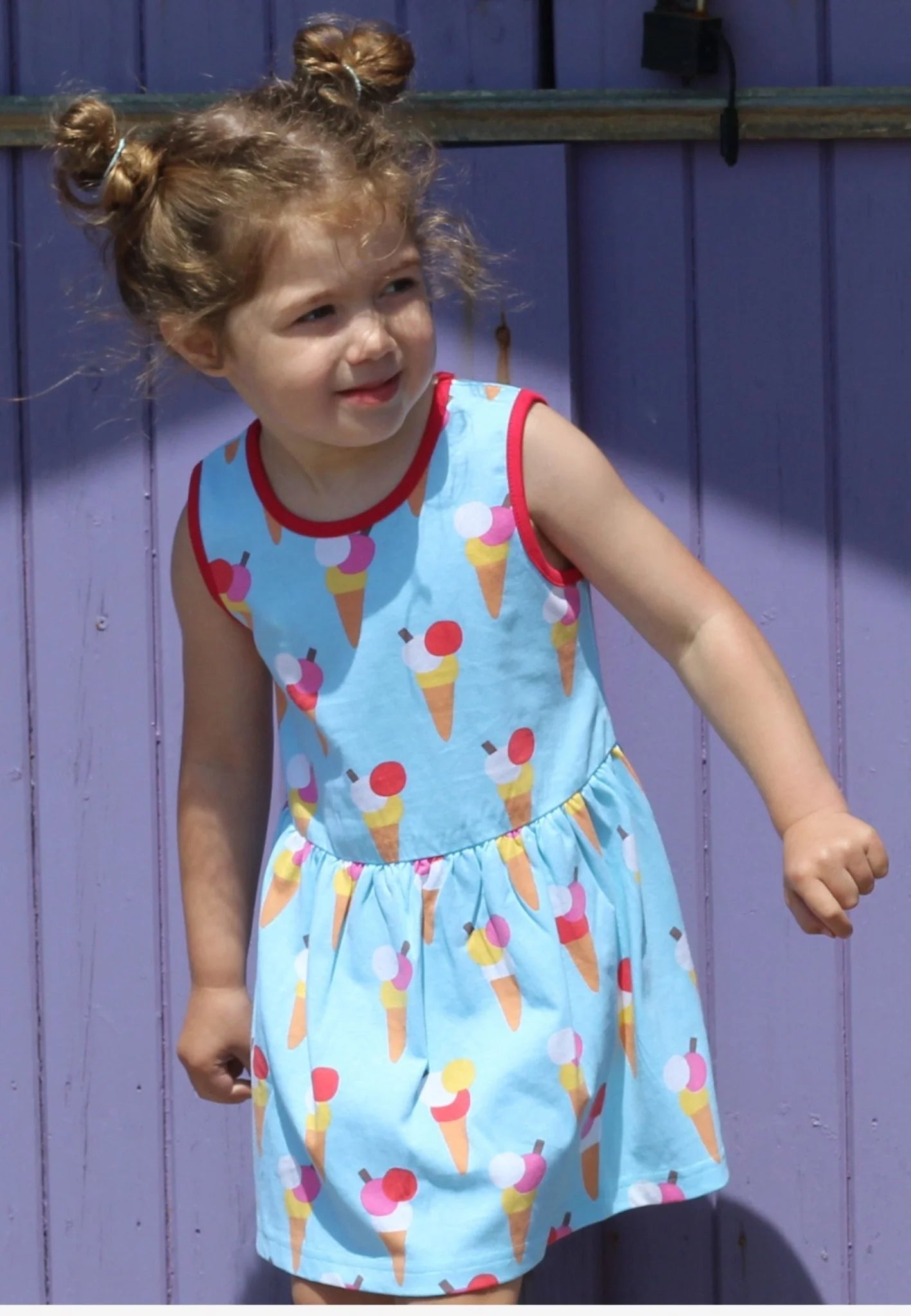 Child wearing a blue dress with ice cream cone pattern against a purple wall