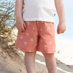Child wearing a white shirt with blue collar, pink shorts, and a pink sun hat on a sandy beach.