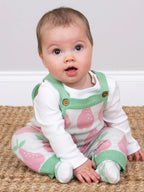 Baby wearing a pink and green outfit with strawberry pattern on a beige rug.