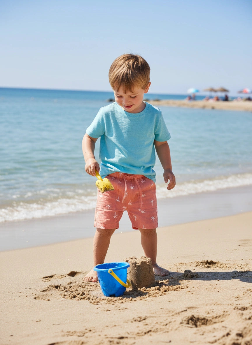Child playing on a sandy beach with a blue bucket and yellow shovel.