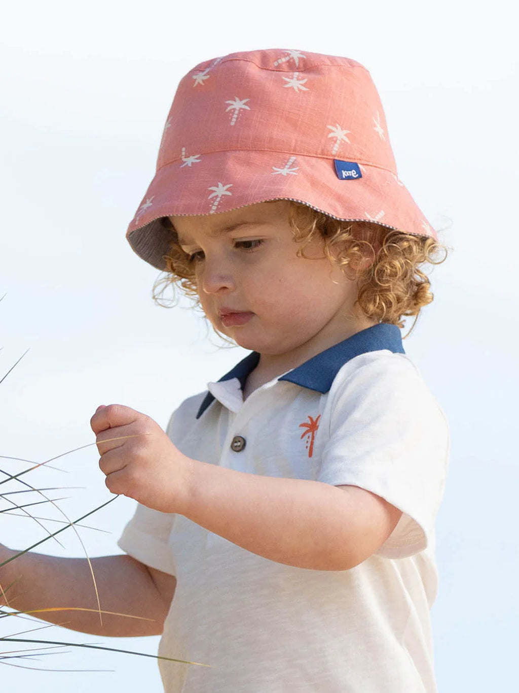 Child wearing a pink bucket hat with white patterns against a clear blue sky.