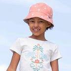 Young girl wearing a white t-shirt with a design, pink skirt, and pink hat outdoors.