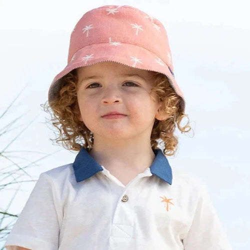 Child in beach attire with a pink hat and white shirt on sandy dunes