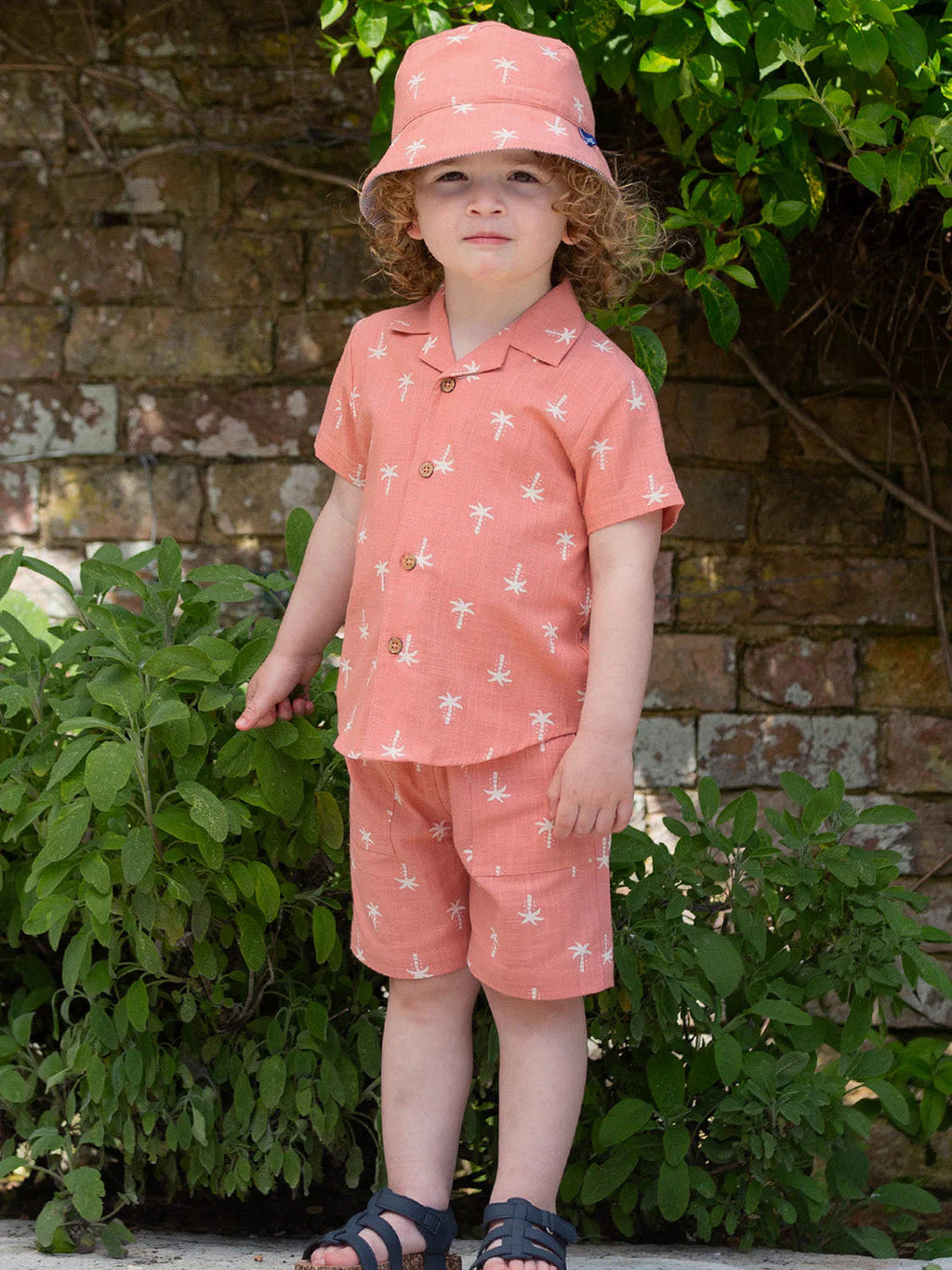 Child wearing a matching pink outfit with white patterns, standing outdoors against a brick wall.