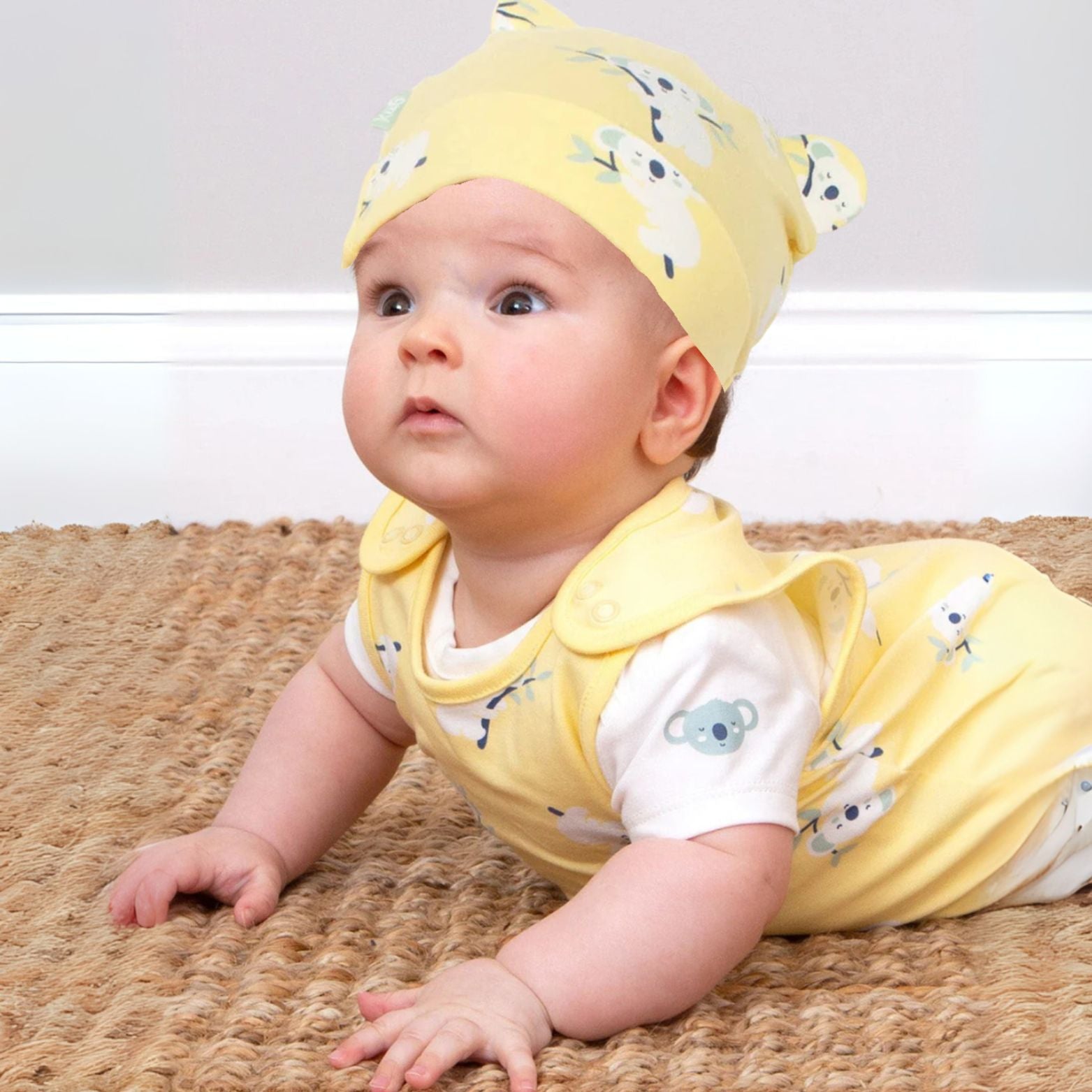 Baby wearing a yellow outfit with animal patterns on a textured surface
