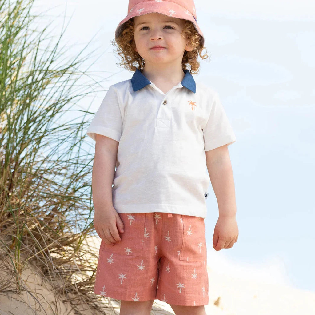 Child in beach attire with a pink hat and white shirt on sandy dunes