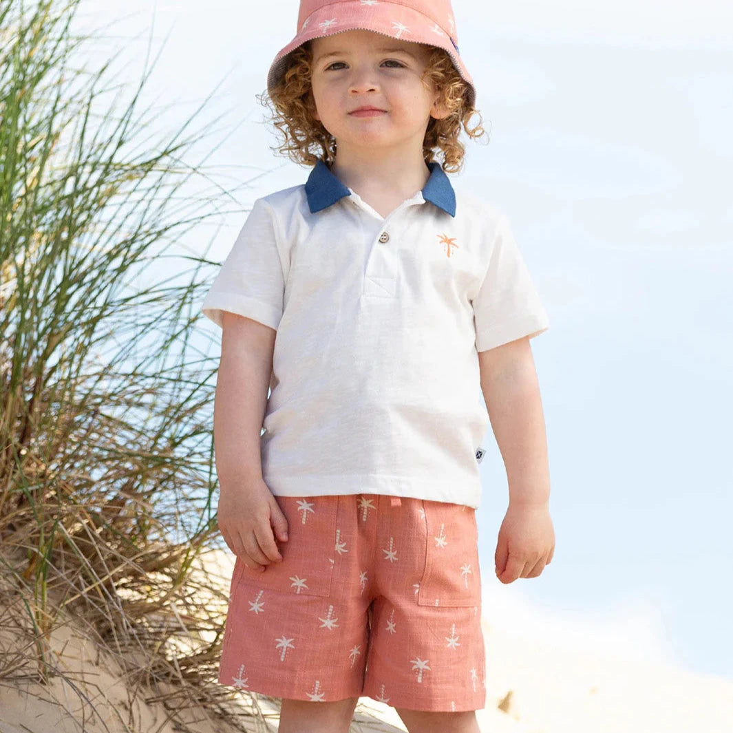 Child in beach attire with a pink hat and white shirt on sandy dunes