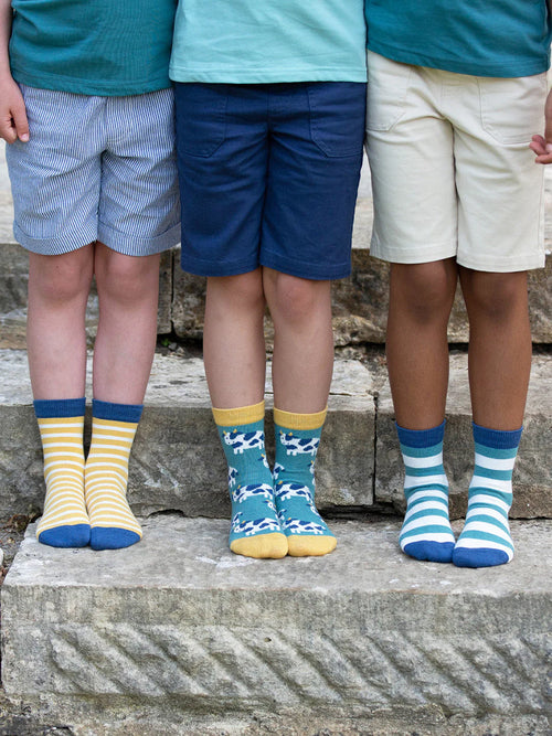 Three children wearing colorful socks standing on stone steps.