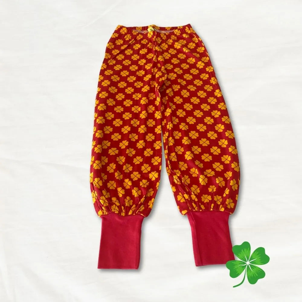 Red and yellow patterned baby pants on a white background with a green clover icon.