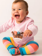 Baby wearing a pink shirt with a cartoon design and colorful socks on a white background
