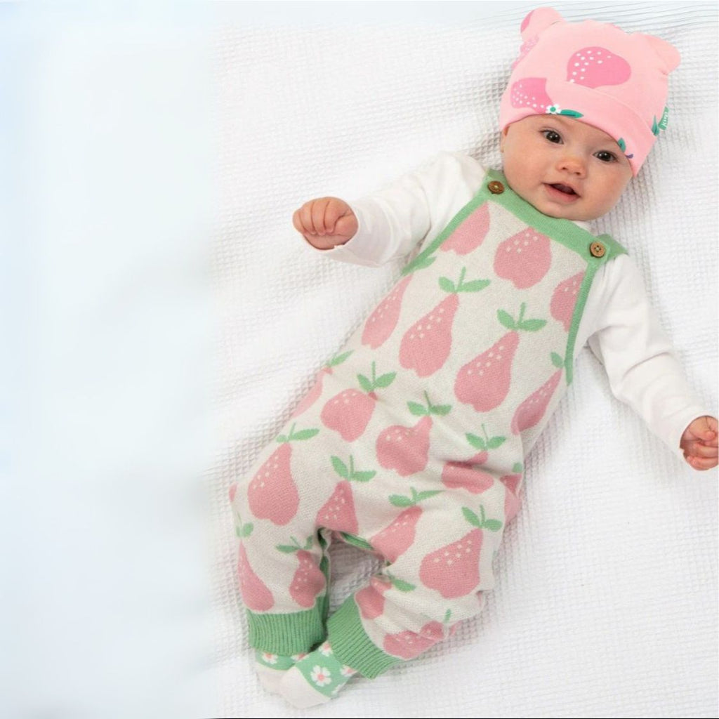 Baby wearing a pink and green outfit with pear pattern on a white blanket