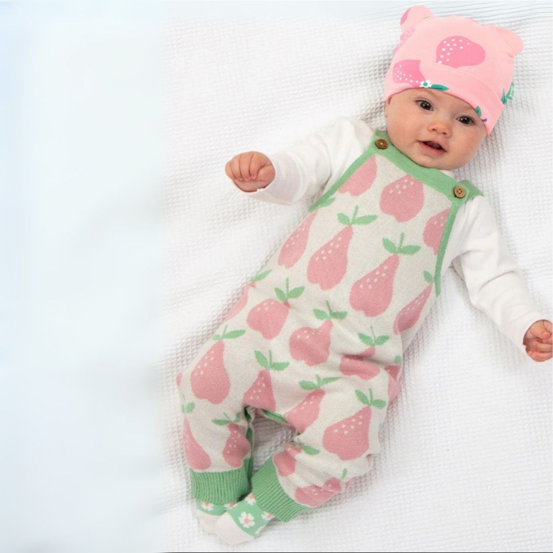 Baby wearing a pink and green outfit with pear pattern on a white blanket