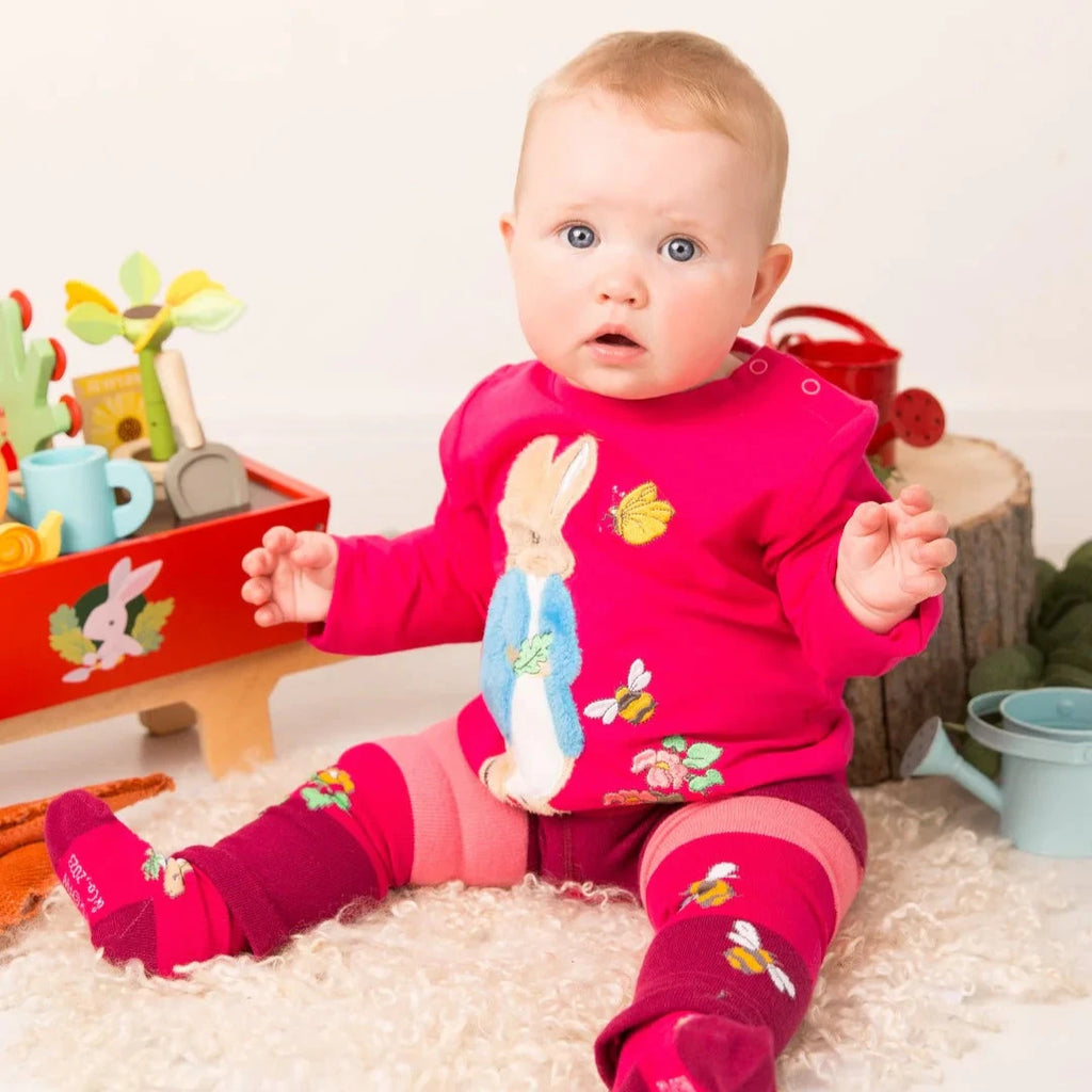 Baby in a pink outfit with animal prints sitting on a white surface.