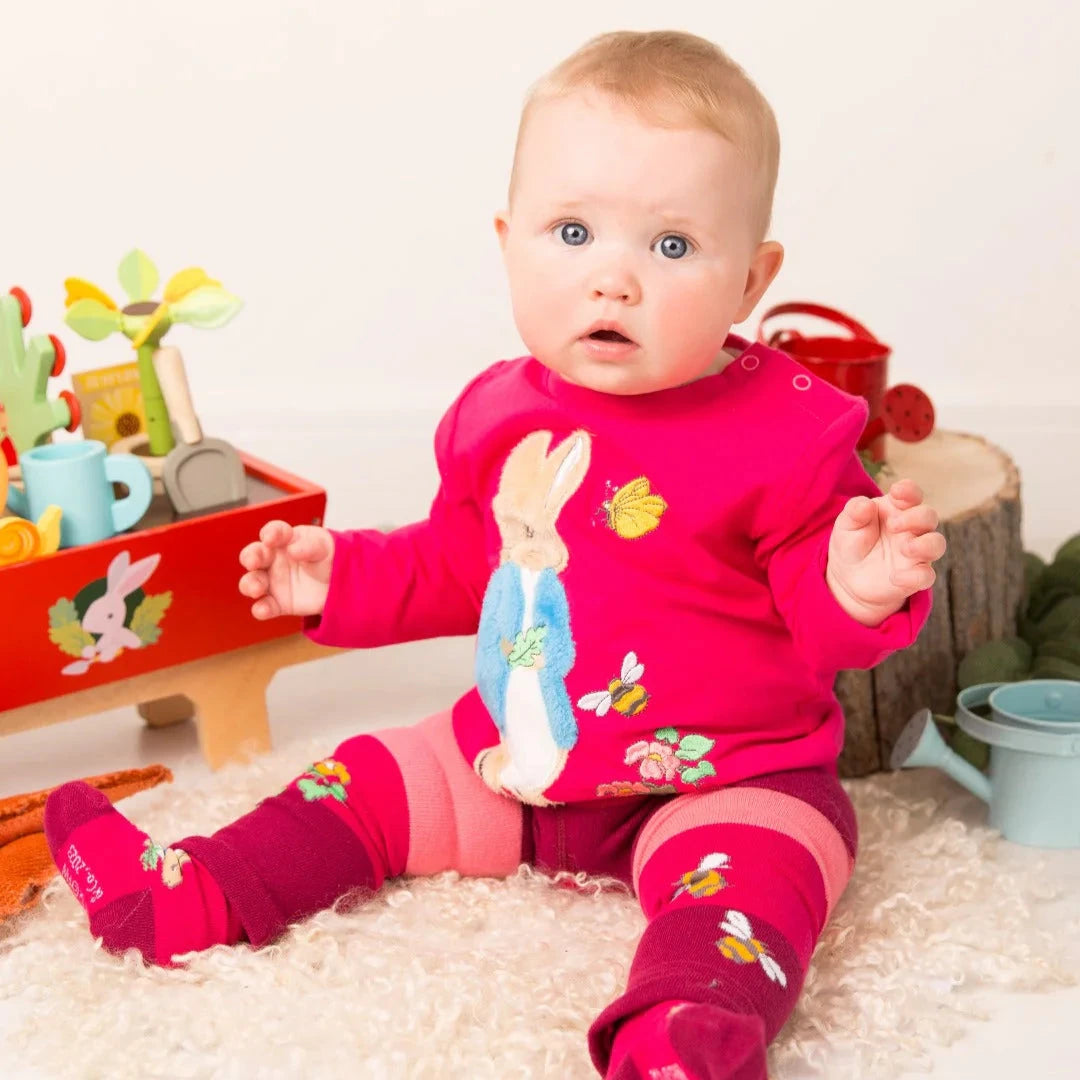 Baby in a pink outfit with animal prints sitting on a white surface.