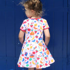Child wearing a colorful dress with fruit pattern standing against a blue wall.