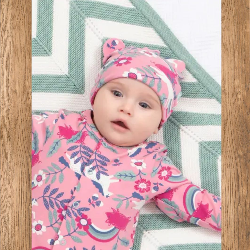 Baby in pink floral outfit and hat on a wooden floor