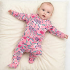 Baby in a pink floral onesie lying on a green and white zigzag patterned rug.