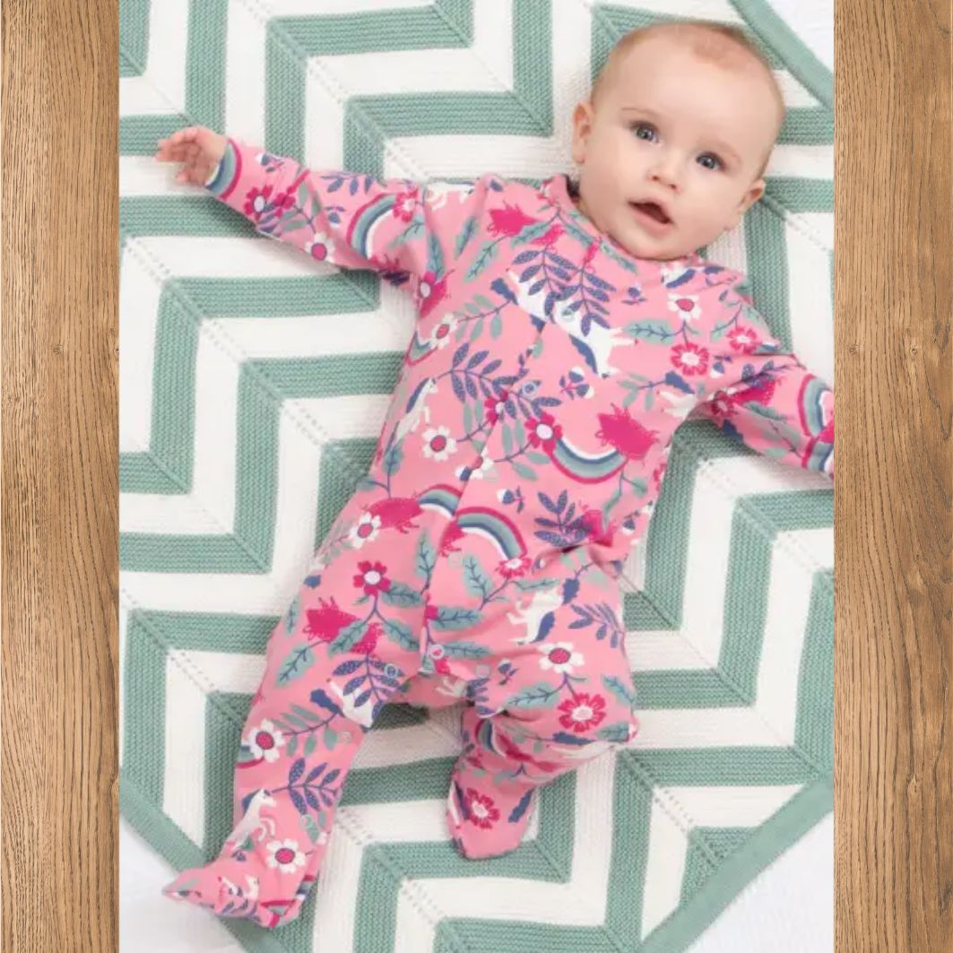 Baby in a pink floral onesie lying on a green and white zigzag patterned rug.