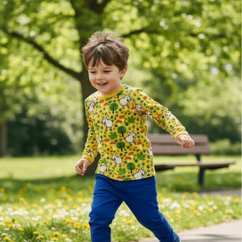 Child in a colorful shirt and blue pants walking on a path with a toy car in a park.