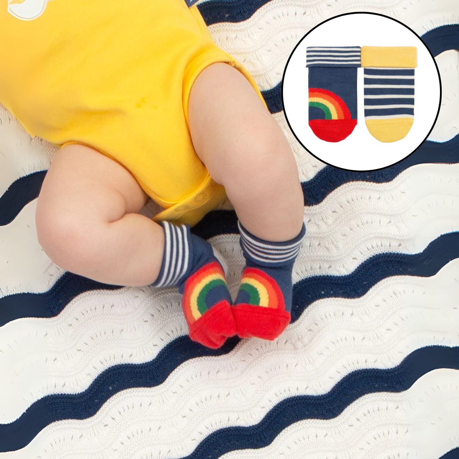 Child wearing colorful socks with rainbow designs on a striped blanket.
