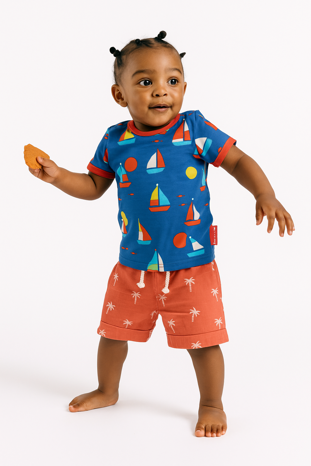 Child wearing a blue shirt with sailboat pattern and orange shorts on a white background