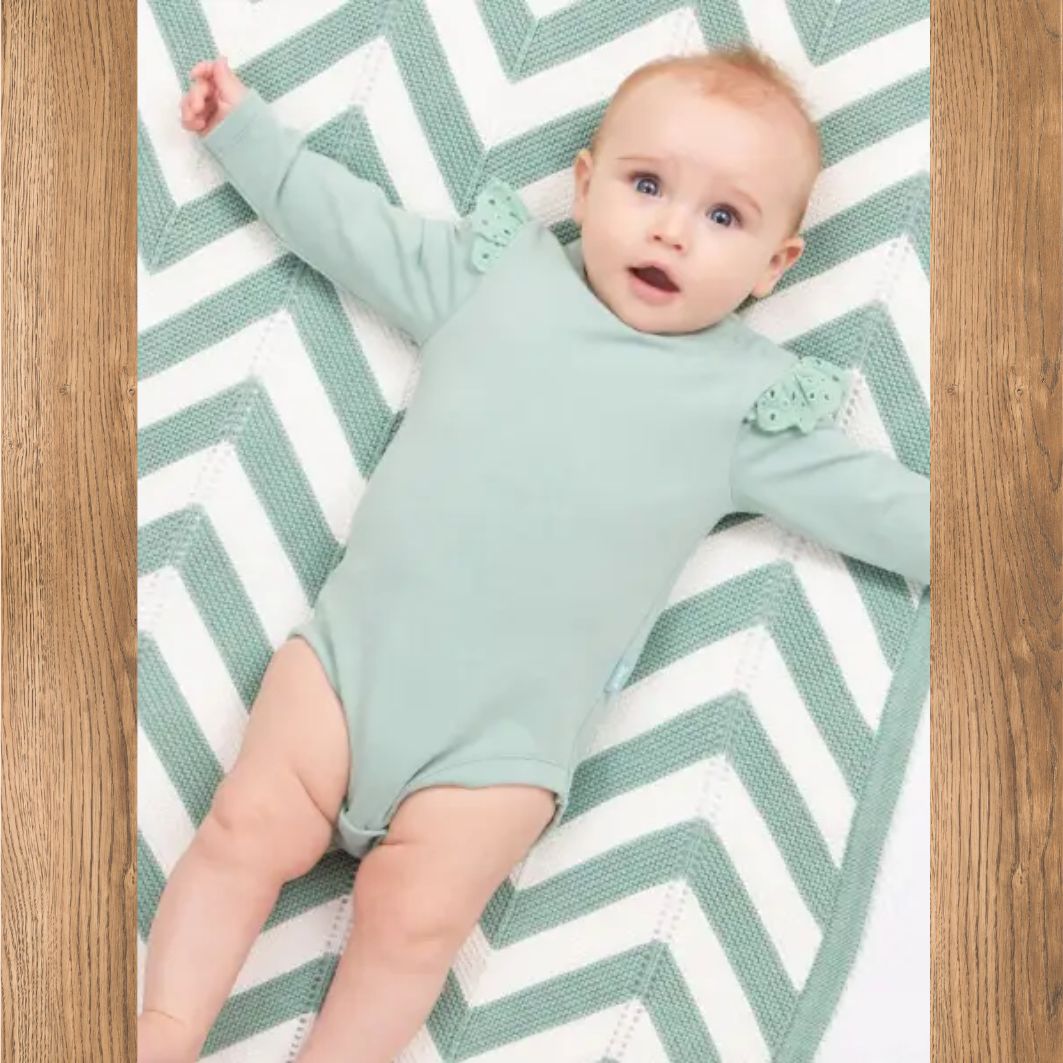 Baby in a light green outfit lying on a chevron-patterned rug.