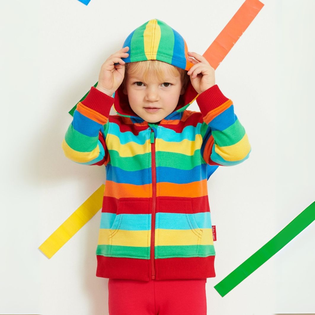 Child wearing a colorful striped hoodie and pants against a white background with colorful stripes.